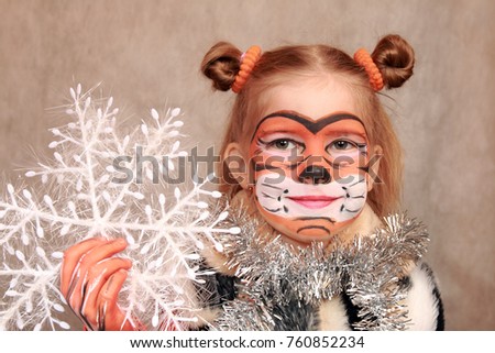 A sweet girl painted like a tiger is holding a Christmas snowflake toy in her hand