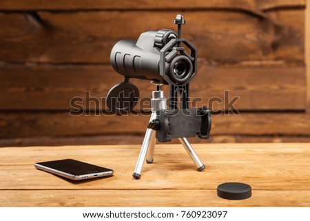 Spotting scope perfect optical equipment for sport, tourism, hunting, wildlife and astronomy zooming. Used with lens caps, tripod, smartphone holder and other accessories. On blurred wooden background