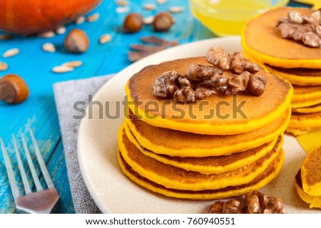 Fragrant golden pumpkin pancakes with honey and walnuts on a blue wooden background. Traditional American dish