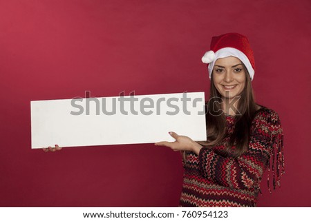 Cute girl wearing a Christmas hat on a red background holding a place for the ad