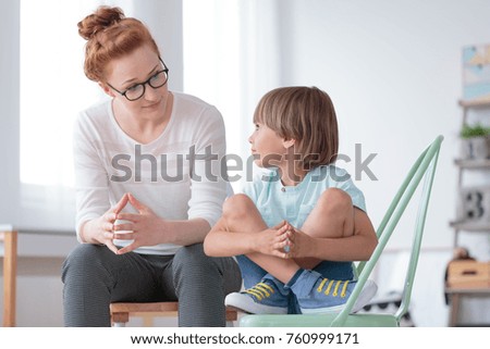 Young female school psychologist having serious conversation with smart little boy at her office Royalty-Free Stock Photo #760999171