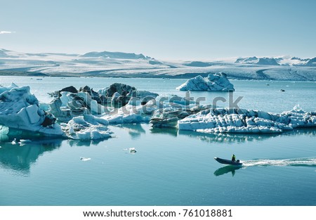 Beautiful vibrant picture of icelandic glacier and glacier lagoon with water and ice in cold blue tones, Iceland, Glacier Bay, icebergs in the water and in the lagoon a motor boat is floating