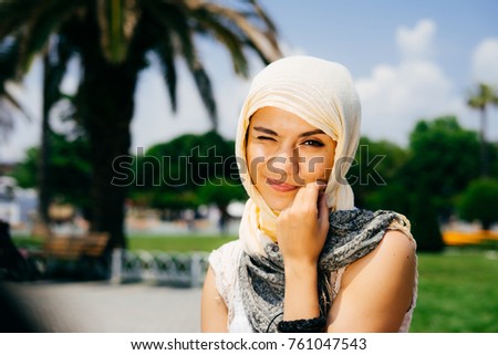 Funny emotional Muslim girl in a scarf sits in the park