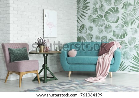 Green table with a plant between pink chair and blue sofa in floral living room with wallpaper and poster Royalty-Free Stock Photo #761064199