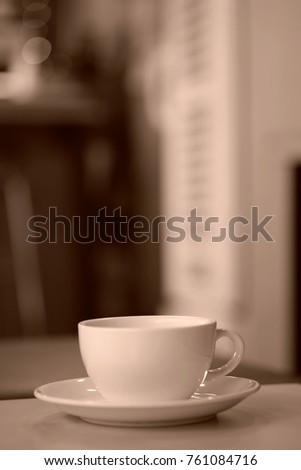  A sepia image of a coffee mug placed on a table in a coffee shop.