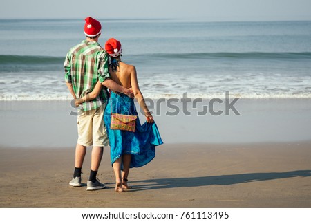 happy couple walking on beach in santa hat