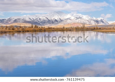 A bright autumn landscape with a beautiful lake, mountains covered with snow, clouds on the blue sky and their reflections