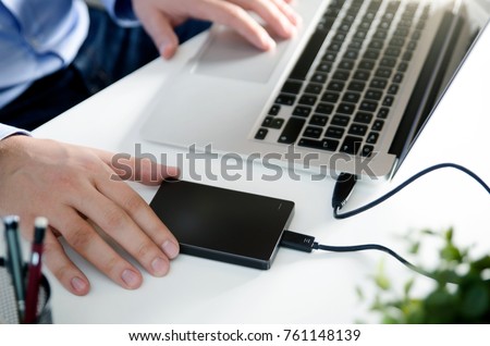External backup disk hard drive connected to laptop. Man with notebook making safety personal data copy. Royalty-Free Stock Photo #761148139