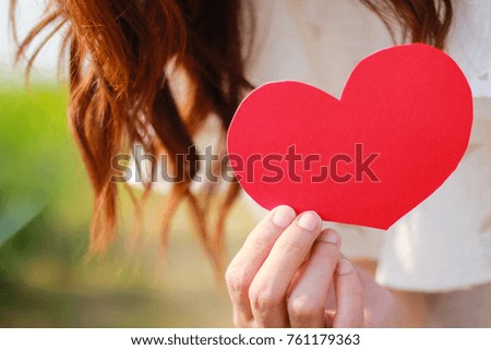 A beautiful woman wearing white dress and  holding a paper red heart. Valentine concept.