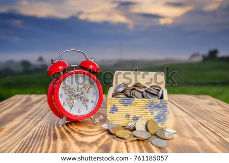 Coins in box and alarm clock  on the pine wood  with beautiful sunrise as background for travel concept.