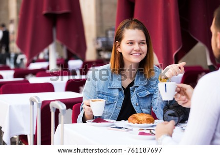 Cheerful man and woman sitting with coffee and talking at the table in street cafe