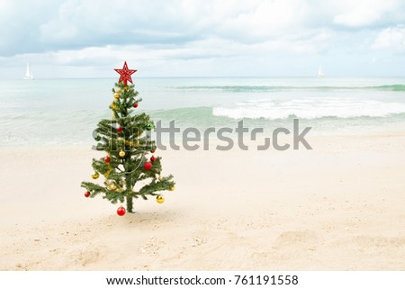 Decorated Christmas tree standing on the sand with ocean and sailboats in the background Royalty-Free Stock Photo #761191558