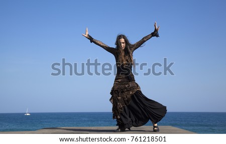famenco by oceaside - slim attractive woman in a black and golden dress dances by oceanside