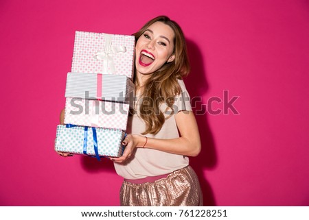 Image of happy young lady standing isolated over pink background holding surprise gifts boxes. Looking camera.