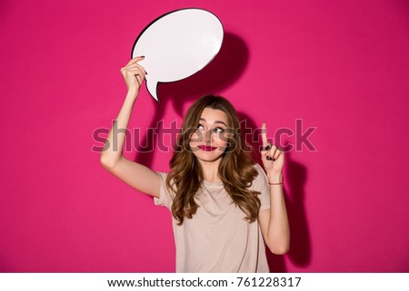 Photo of cheerful pretty young woman standing isolated over pink background. Looking aside holding speech bubble over head have an idea pointing.