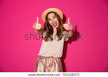 Picture of excited young woman in hat standing isolated over pink background. Looking camera showing thumbs up gesture.
