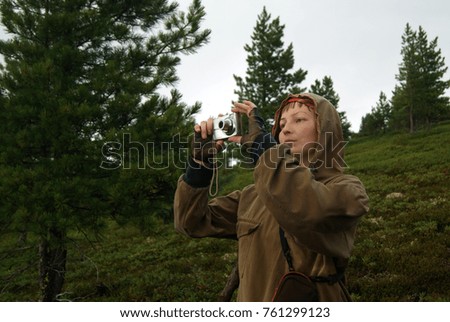 traveller girl in field clothes in the rain takes a picture with a point-and-shoot camera on the mountainside