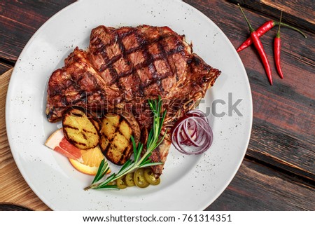 A large steak with spices and vegetables on the grill
