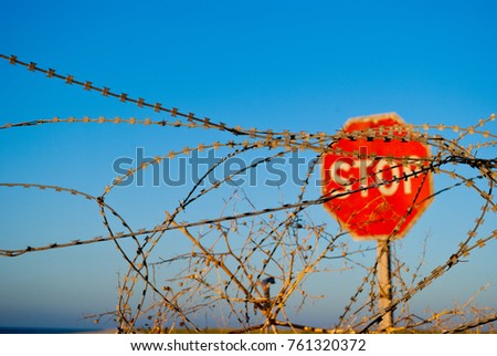 a large red road prohibiting stop sign stands on a deserted beach in front of him fence of metal wire fence wooden poles passage forbidden yellow sand blue sea shore clear blue sky summer warmth