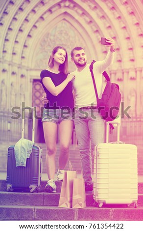 happy american female and male standing with baggage at street and taking selfie 