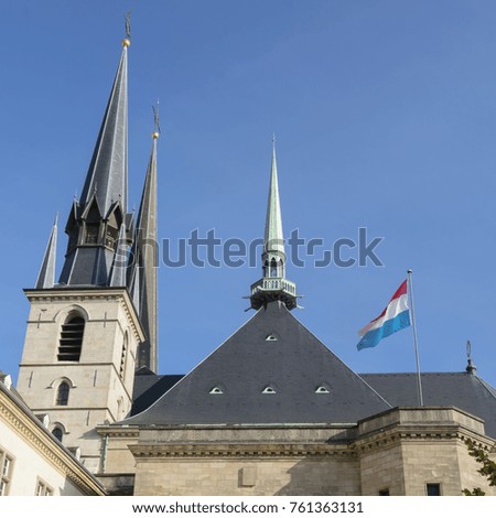 Luxembourg flag against blue sky in front of Cathedral of Our Lady of Luxembourg.