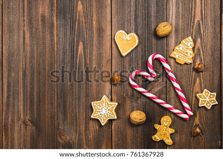 Christmas candy canes, gingerbreads of different shapes, hazelnuts, walnuts on a brown wooden table. Copy space
