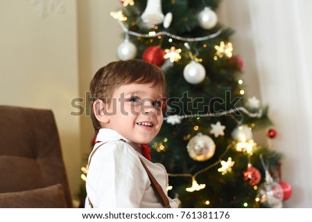Child wait a New Year. Happy boy sit on couch under a Christmas tree. Portrait of a happy boy