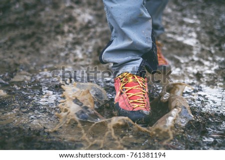 Detail of trekking waterproof boots in a mud. Muddy hiking boots and splash of water. Man splashing in muddy and water in the countryside.