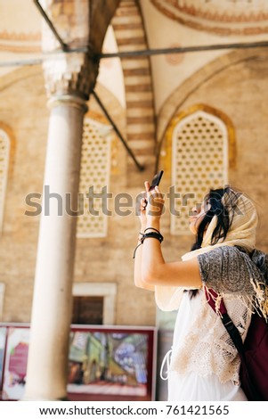 A young woman in a scarf takes pictures in the courtyard of the mosque on the phone