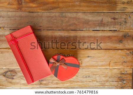 Red gift box and red ribbon and mini heart inside on wood background with space.