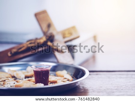 Close-up of a wine glasses  with bread in communion plate with blurred of crucifix of Jesus on the bible, christian background with copy space