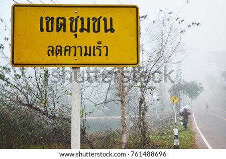 Thai people carrying sack walking at beside road with traffic sign City Limit Reduced Speed at Ban Bo Kluea village in Nan, Thailand (thai text on board translation mean City Limit Reduced Speed)