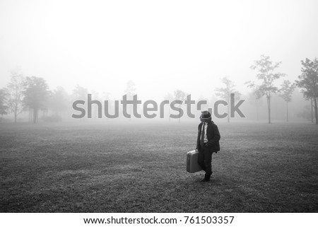 Asian business man walks with suitcase in the misty field, black and white photography