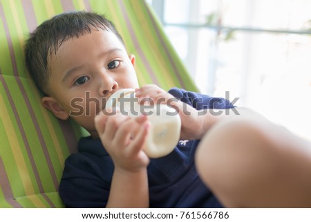 Happy toddler little boy laying sucking bottle bottle with smiling face and looking at the camera.