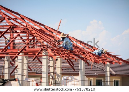 Construction welder workers installing steel frame structure of the house roof at building construction site with clouds and sky