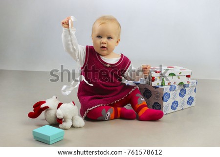 Holidays, Birthday, Children and people concept.Shot of a little adorable baby girl opening presents and playing toys. An Adorable Baby Girl in red dress playing with Christmas Gifts.