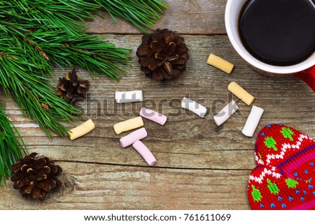 Christmas background with fir tree, cup of coffee and mittens on a wooden table.