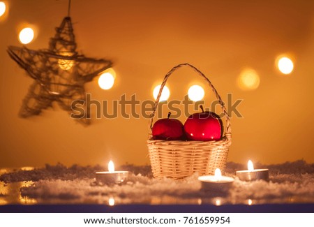 Christmas background with basket with red apples, candles, snow, stars and bokeh lights 
