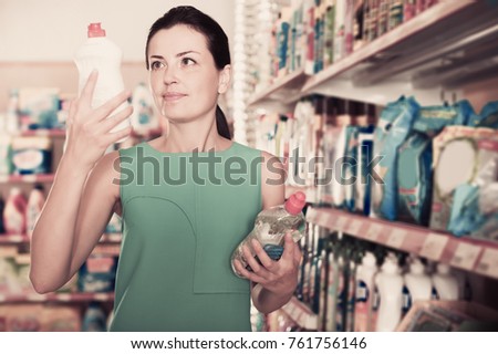 Portrait of glad adult woman choosing dishwashing liquid at the supermarket