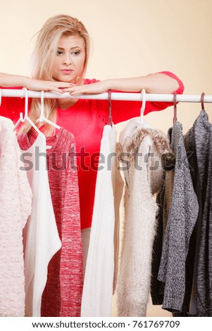 Fashionable style, trendy clothes, thinking about clothing concept. Blonde woman standing in wardrobe picking perfect winter outfit.