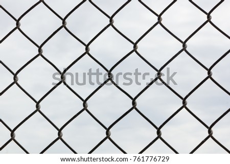 Viewing clouds through a chain link fence at a baseball field from the dugout. Closeup on the chain link fence.