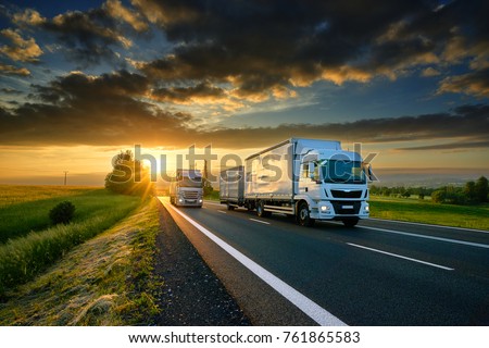 Overtaking trucks on an asphalt road in a rural landscape at sunset Royalty-Free Stock Photo #761865583