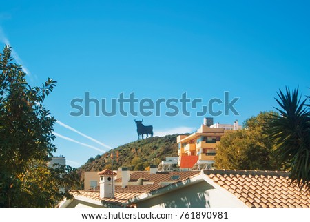 Toro Osborne, iconic symbol of Spain, silhouette of black bull on the hill over Fuengirola town, houses with tile roofs at the foreground.