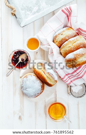 Tea time with festive sufganiyot donuts filled with jelly and covered with sugar powder. White wooden background, bright lighting. Vertical composition.