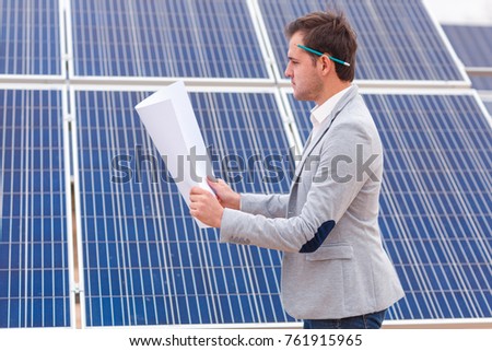 The chief looks at the project in his hands against the background of solar panels