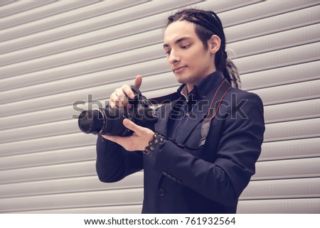 A handsome young guy, a photographer, looks at the camera, takes aim, takes pictures. Shoot, snapshot. A man with dreadlocks. Copy space.