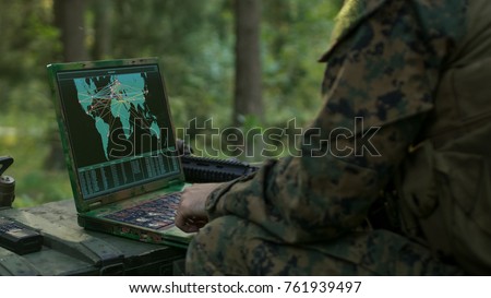 Military Operation in Action, Soldiers Using Military Grade Laptop Use Military Industrial Complex Hardware for Accomplishing International Mission. In the Background Camouflaged Tent on the Forest.