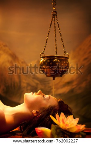 Spa salon: Beautiful Young Woman having Shirodhara - Ayurveda Oil Massage in India Spa Salon with Lotus Royalty-Free Stock Photo #762002227