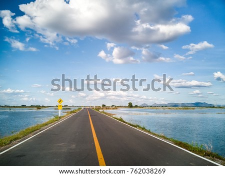 Asphalt road in the countryside through a large lagoon, and there are traffic signs to use the speed limit of 15km / hr.