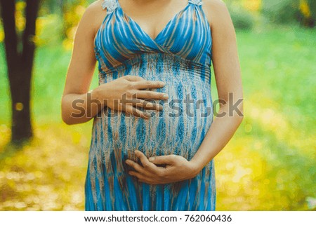 Closeup on tummy of pregnant woman, wearing long green dress, outdoors, new life concept